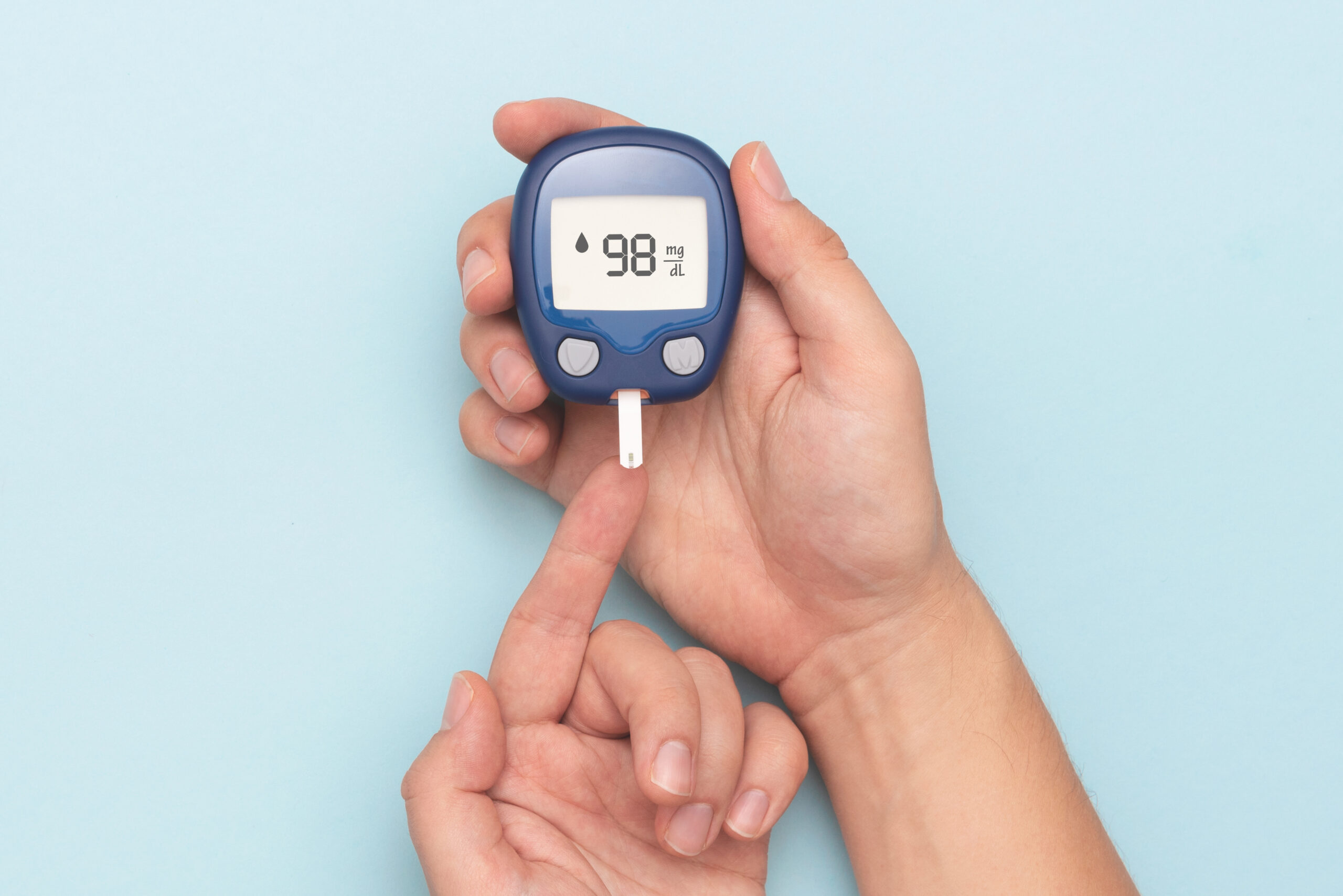 Man using glucometer, checking blood sugar level. Diabetes concept on blue background